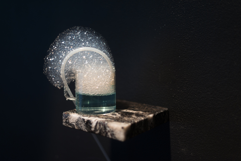 Closeup of a teacup on a marble shelf containing a blue liuquid and overflowing with bubbles.